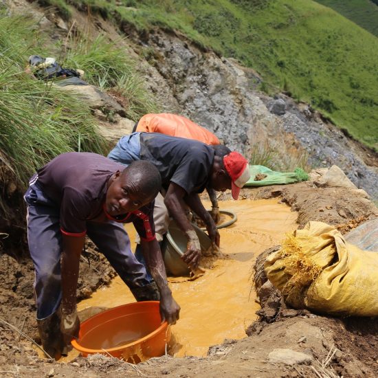 Small-scale gold miners dip buckets into a small mountain pond to collect silt as part of the mining process.