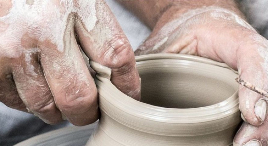 A person sculpts a clay pot with their finger.