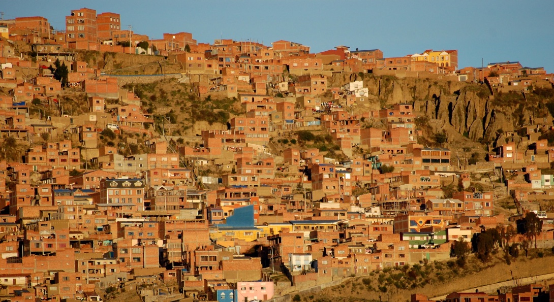 Sunset in La Paz, Bolivia casts a golden light over numerous brick homes lining a mountainside in the city.