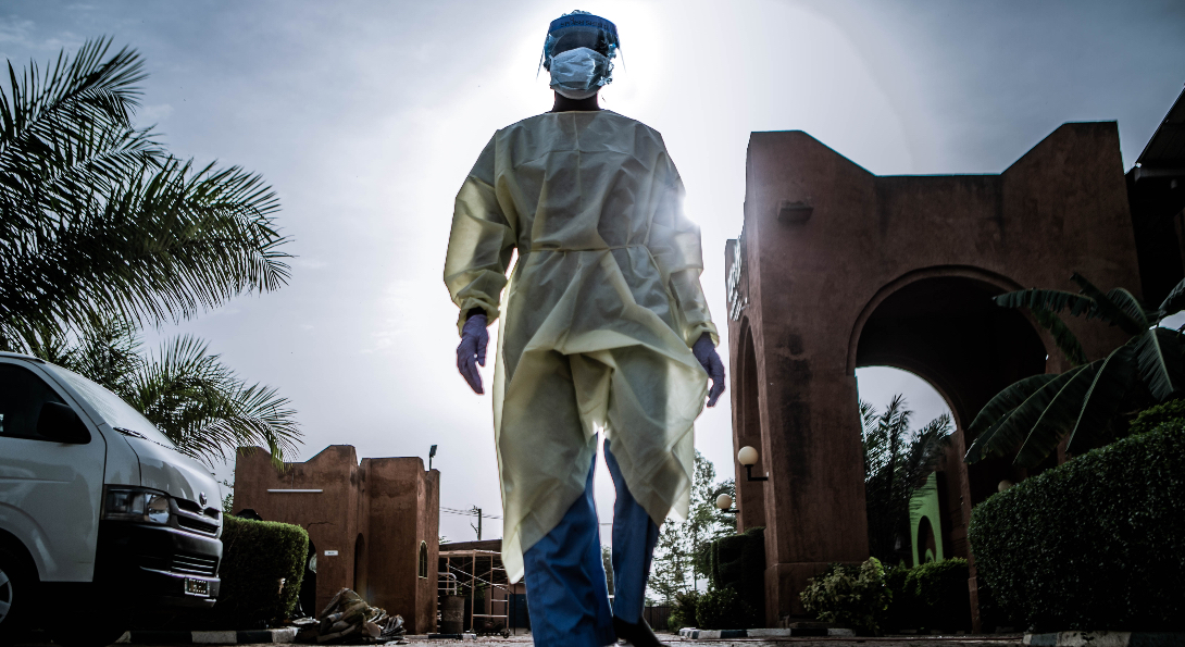A healthcare professional wearing full personal protective equipment walks along a street near a hospital during the COVID-19 pandemic.