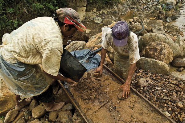Two artisanal miners sift through silt and rocks in a trough full of water.